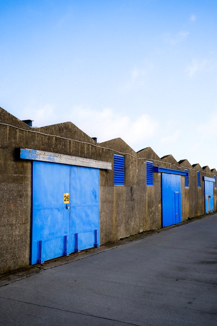 Row of industrial blue doors on warehouse buildings with blue sky background.