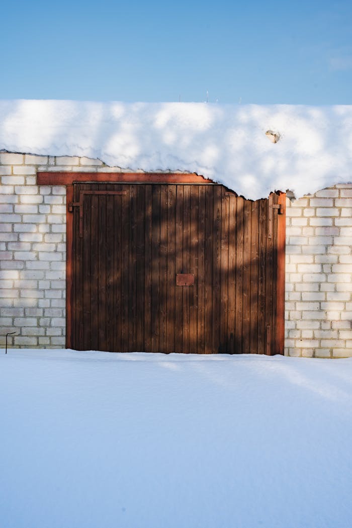 Services A wooden garage door framed by brick walls under a clear blue sky with fresh snow.